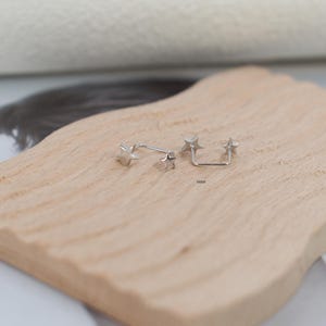 Puede incluir: Un par de pendientes plateados con dise&ntilde;o de estrella. Un pendiente consiste en un perno de estrella individual, mientras que el otro es un pendiente de doble extremo con una estrella en cada punta conectadas por una fina barra met&aacute;lica en forma de U.