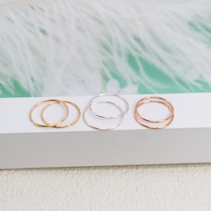 May include: A set of six thin, circular metal rings arranged in three pairs. The collection includes two gold-toned rings, two silver-toned rings, and two rose gold-toned rings. Each ring features a simple, continuous band design with a smooth finish.