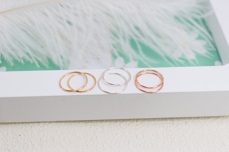 May include: A set of six thin, circular metal rings arranged in three pairs. The collection includes two gold-toned rings, two silver-toned rings, and two rose gold-toned rings. Each ring features a simple, continuous band design with a smooth finish.