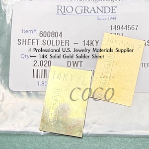 May include: Sheet solder labeled "14KY" and "14K Solid Gold Solder Sheet" from Rio Grande, a U.S. jewelry materials supplier. The image shows two small, rectangular pieces of gold-colored metal, with text and markings.