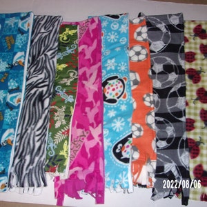 May include: Assortment of eight fleece fabric strips with various patterns, including a blue and white snowflake pattern, a black and white zebra pattern, a green and yellow lizard pattern, a pink and white camouflage pattern, a blue and white snowflake pattern with a penguin, an orange and white soccer ball pattern, a black and white soccer ball pattern, and a green and white ladybug pattern.