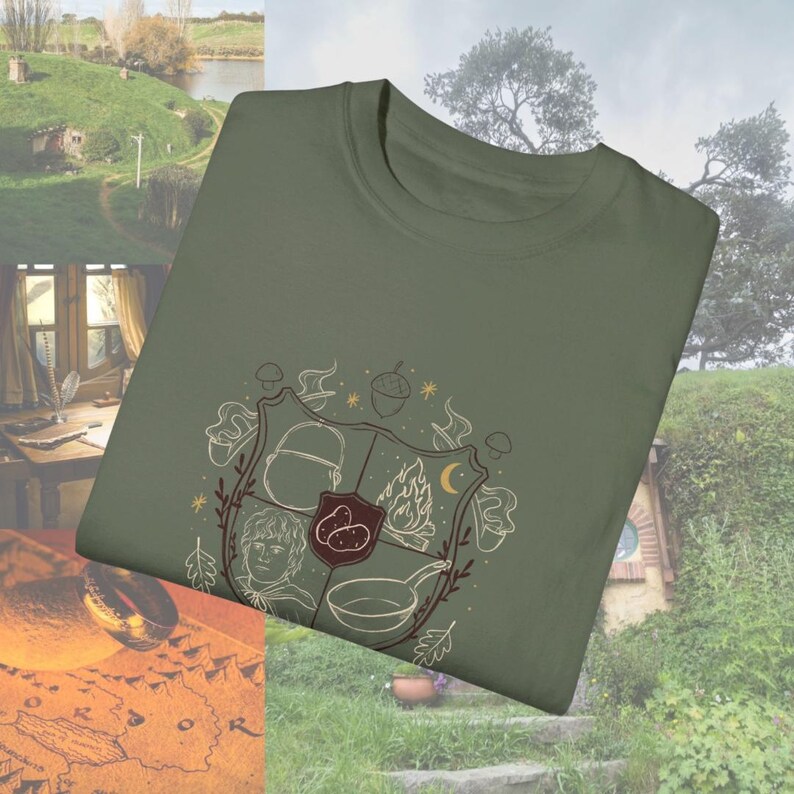May include: A green t-shirt with a brown and white illustration of a coat of arms. The coat of arms features a mushroom, a fire, a crescent moon, a pot, and a hobbit. The text "The Shire" is visible on the t-shirt.