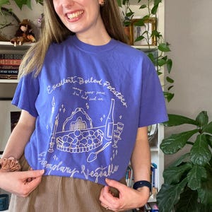 Puede incluir: Una camiseta morada con un diseño gráfico blanco de un plato de patatas hervidas, una botella de vino y dos copas de vino. El texto de la camiseta dice "Excellent Boiled Potatoes" y "Templary Vegetable".