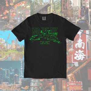 May include: Black t-shirt with a green graphic print of a knife and the text "NO PEAK" with the words "ON MY HONOR, MY LIFE, AND MY JADE" underneath.