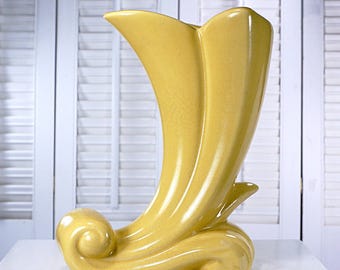May include: A yellow ceramic vase with a unique, curved design. The vase features a flared top and a base with a swirling, wave-like detail. The vase is approximately 12 inches tall.