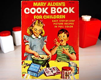 May include: A vintage red and white cookbook titled "Mary Alden's Cook Book for Children" with a picture of two children baking. The book has the text "Easy Step-by-Step Picture Recipes in Full Color" on the cover.