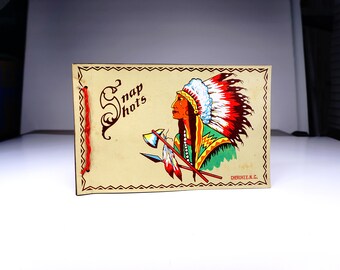 May include: Vintage souvenir photo album with a Native American illustration. The cover features a profile of a Native American in a headdress, crossed tomahawks, and the words "Snap Shots". The album is bound with red string and has the text "CHEROKEE, N.C."