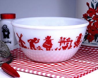 May include: White mixing bowl with a red and white gingham pattern on a red and white checkered cloth. The bowl has a red silhouette design of a windmill, people, and ducks. A white container with a red lid is in the background.