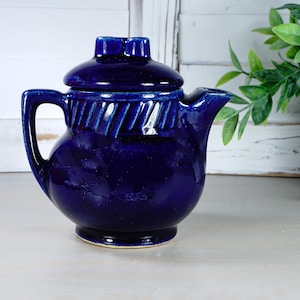 May include: A cobalt blue ceramic teapot with a lid and a twisted design around the middle. The teapot has a handle and a spout.