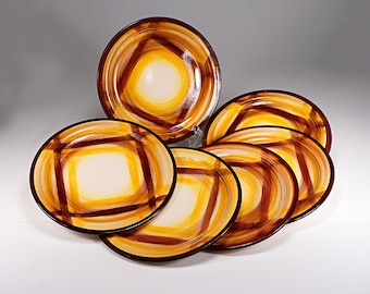 May include: A set of six ceramic plates with a unique design. Each plate features a cream-colored center, surrounded by concentric rings of yellow, orange, and brown, with a dark brown rim. The plates are arranged on a white surface.