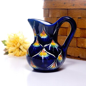 Peut inclure: Un petit pichet en céramique bleu avec un motif floral blanc et jaune. Le pichet a un corps rond et une anse.