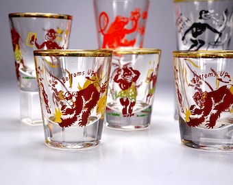 May include: Set of vintage shot glasses with gold rims. Each glass features a different cartoon monkey illustration in red, yellow, and black. The phrase "Bottoms Up" is printed on some of the glasses.