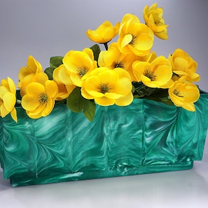 May include: A green and white marbled ceramic planter with a fluted design, filled with a bouquet of yellow flowers.