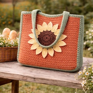 Può includere: Una borsa tote all'uncinetto nei toni dell'arancione, verde e giallo. La borsa presenta un'ampia applicazione di girasole sul davanti. I manici e il bordo sono verdi. La borsa è appoggiata su una panca di legno.