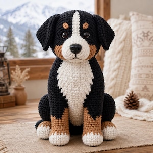 Puede incluir: Un peluche de perro de montaña de Berna tejido a ganchillo con un patrón de colores negro, blanco y tostado. El juguete tiene una mancha blanca en la cara, pecho blanco, marcas tostadas sobre los ojos y en las patas, y pies blancos con ojos oscuros.