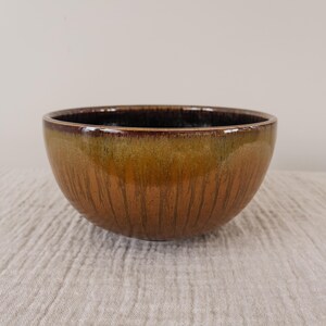 May include: A brown ceramic bowl with a dark brown rim and a light brown glaze. The bowl has a textured surface and is slightly wider at the top than the bottom.