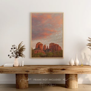 May include: A framed photograph of red rock formations against a pink and purple sunset sky. The image is displayed on a wooden table with dried pampas grass in vases.