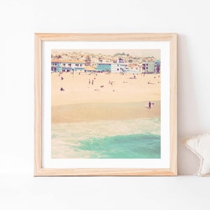 K&ouml;nnte beinhalten: Ein gerahmtes Foto einer Strandszene mit bunten H&auml;usern im Hintergrund, einem Sandstrand und t&uuml;rkisfarbenem Wasser mit Wellen, die an den Strand brechen.