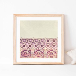 K&ouml;nnte beinhalten: Ein gerahmter Druck eines Vintage-Fotos eines Geb&auml;udes mit einer gemusterten Fassade. Das Geb&auml;ude ist mit einem sich wiederholenden Muster aus geometrischen Formen in Rosa-, Lila- und Wei&szlig;t&ouml;nen verziert. Der Druck wird an einer wei&szlig;en Wand mit einem beigefarbenen sternf&ouml;rmigen Kissen im Vordergrund gezeigt.