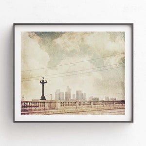 May include: A vintage-style photograph of a cityscape with a bridge and a streetlight in the foreground. The sky is cloudy and the city skyline is visible in the distance.