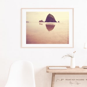 May include: A vintage-style photograph of Haystack Rock, a large sea stack located on the Oregon coast, with its reflection in the water. The photo has a warm, golden tone.