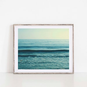 May include: A framed photograph of a blue ocean with waves crashing on the shore. The photo is in a light wood frame.
