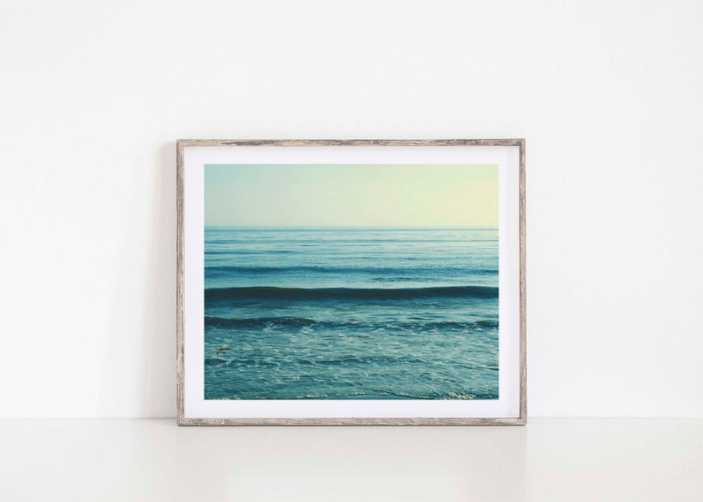 May include: A framed photograph of a blue ocean with waves crashing on the shore. The photo is in a light wood frame.
