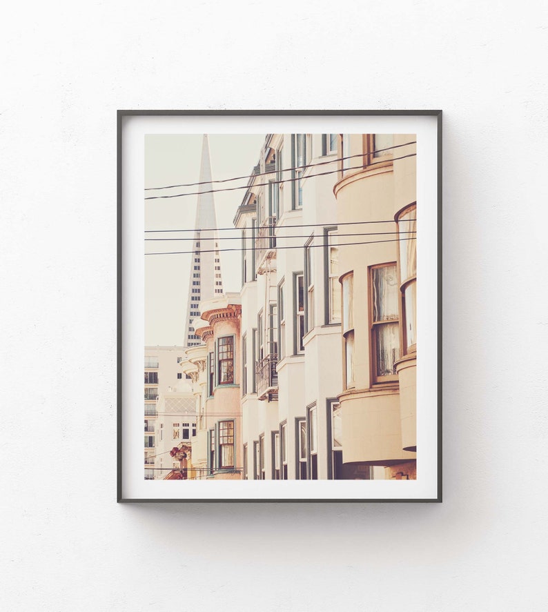 May include: A photograph of a row of colorful buildings in a city. The buildings are tall and narrow, with many windows. The buildings are painted in shades of pink, yellow, and white. A tall building is visible in the background.