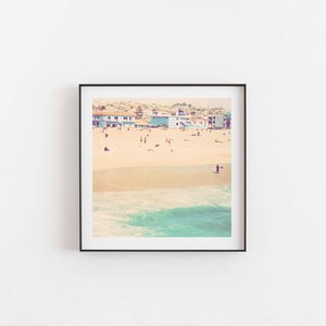 K&ouml;nnte beinhalten: Ein Vintage-Foto einer Strandszene mit bunten H&auml;usern im Hintergrund, einem Sandstrand und einer Person, die im Meer surft.