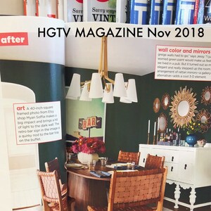 May include: A dining room with a dark green wall, a white buffet, and a wooden table with four chairs. The chairs are made of woven leather and have a natural brown color. The table is round and has a dark wood finish. The buffet has a white finish and has a white countertop. The wall is decorated with a gallery of round mirrors and a large framed photo of a bar sign. The photo is 40 inches square and is framed in a black frame. The mirrors are all different sizes and shapes and are made of rattan. The room is decorated in a mid-century modern style.