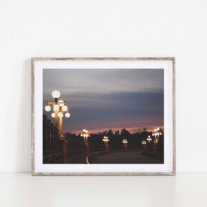 May include: A photograph of a street lined with lampposts at dusk. The lampposts are lit, casting a warm glow on the street. The sky is a soft purple and pink, with clouds in the distance.