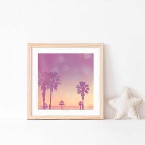 Op de afbeelding: Vierkantige ingelijste print met een zonsondergang met silhouetten van palmbomen. De lucht gaat over van paars naar oranje, met bokeh-lichten. Een beige stervormig kussen ligt rechts.