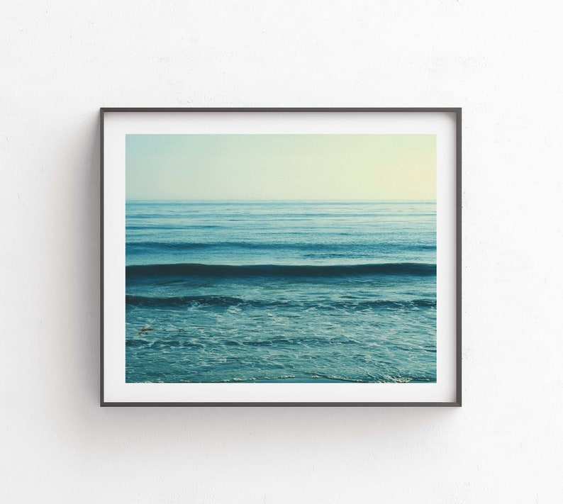 May include: A framed photograph of a blue ocean with waves crashing on the shore. The sky is a light blue and the water is a deep blue.