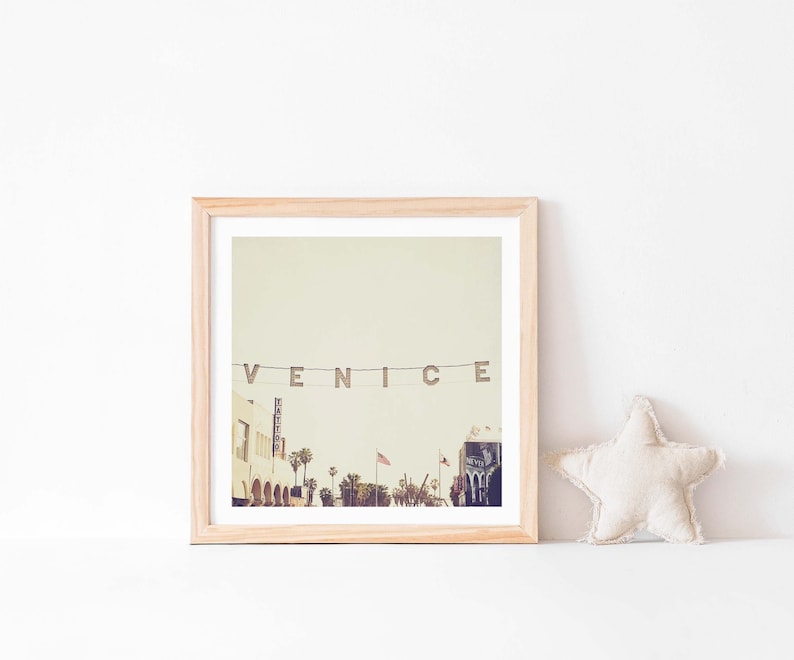 May include: A framed photograph of a street scene in Venice, California. The photo shows a street lined with buildings, palm trees, and a sign that reads "VENICE".