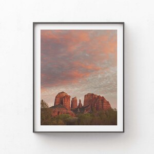 May include: A scenic photograph of red rock formations in the desert with a cloudy sky at sunset. The sky is a mix of pink, orange, and grey.