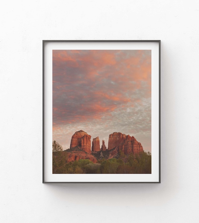 May include: A scenic photograph of red rock formations in the desert with a cloudy sky at sunset. The sky is a mix of pink, orange, and grey.