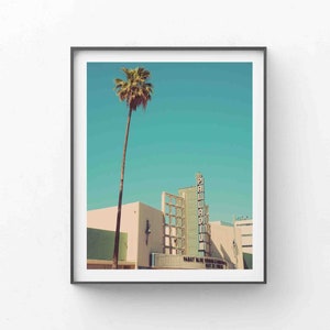 May include: A vintage photograph of a building with a palm tree in front of it. The building has a sign that says "Palladium" and "Past Blue Train & Company May 23-June 1". The sky is a bright blue.