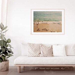 May include: A vintage-style photograph of a beach scene with people swimming in the ocean. The photo has a warm, faded color palette and a soft focus.
