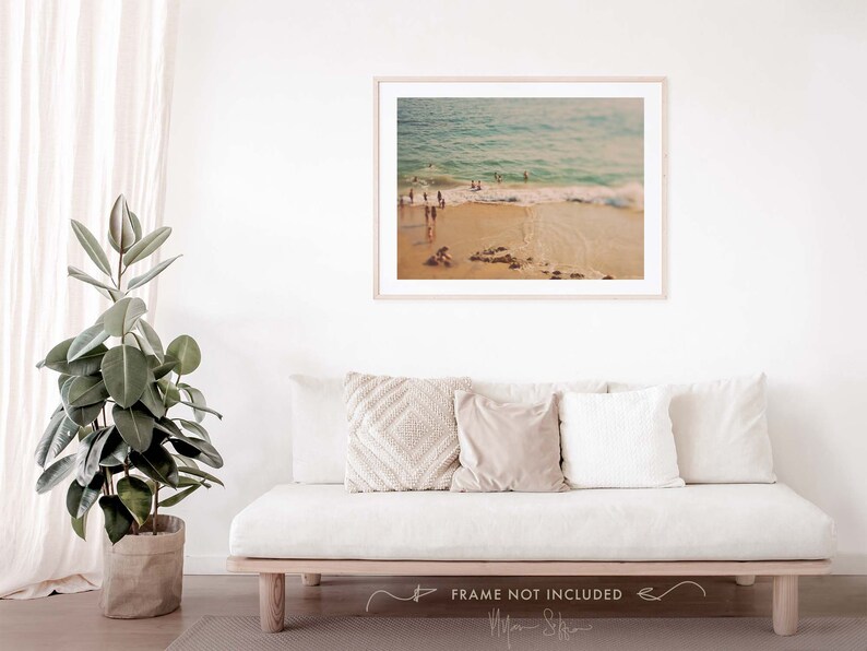 May include: A vintage-style photograph of a beach scene with people swimming in the ocean. The photo has a warm, faded color palette and a soft focus.