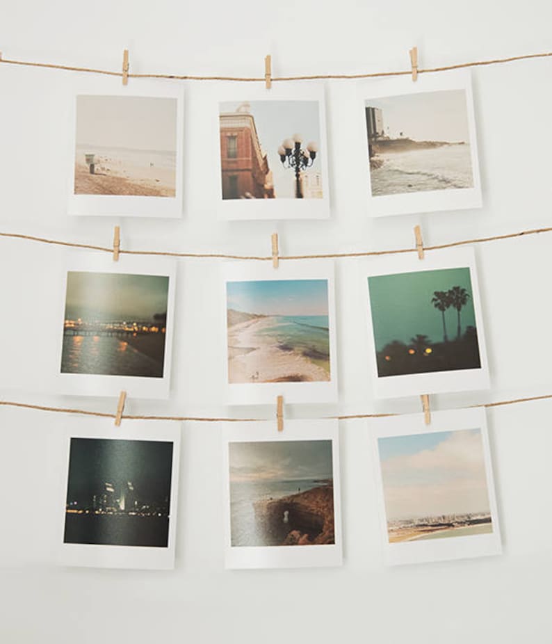 Puede incluir: Una cuerda con nueve fotos colgadas en una pared blanca, cada foto est&aacute; sujeta por una pinza de madera. Las fotos son de diferentes tama&ntilde;os y muestran varias escenas, incluyendo una playa, una calle de la ciudad y una palmera.