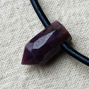 Puede incluir: Un colgante de cristal morado en un collar de cordón de cuero negro.