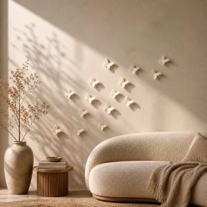 Könnte beinhalten: Eine Ansammlung kleiner, cremeweißer Schmetterlings-Wandaufkleber, die in einem verstreuten Muster an einer schlichten Wand angebracht sind. Die Schmetterlinge sind dreidimensional mit leicht angewinkelten Flügeln.