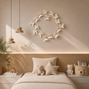May include: A wall display of off-white three-dimensional butterfly cutouts arranged in a circular pattern above a bed. The bed features a beige quilt, a square pillow, and a star-shaped pillow, flanked by two nightstands with a teddy bear and a bear-shaped basket.