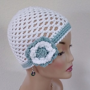May include: White crochet hat with a light blue crocheted flower on the side. The hat has a white and light blue trim.