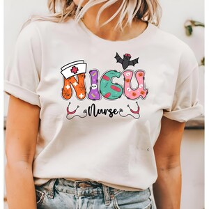 May include: White t-shirt featuring a Halloween-themed graphic that reads "NICU Nurse". The letters are decorated with stitches, a skull, a spiderweb, a bat, and a pumpkin.