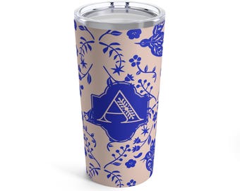 May include: A stainless steel tumbler with a light pink background and a blue floral pattern. The letter "A" is in a blue square in the center of the tumbler.