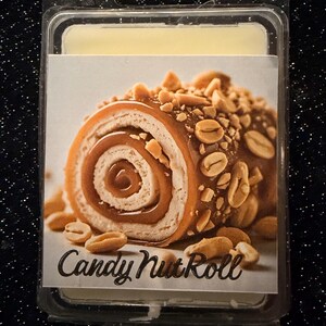 Könnte beinhalten: Ein Wachsschmelz in einer transparenten Kunststoffverpackung. Das Etikett zeigt ein detailliertes Bild einer Candy Nut Roll, mit Erdnüssen und Karamell. Der Text "Candy Nut Roll" ist aufgedruckt.
