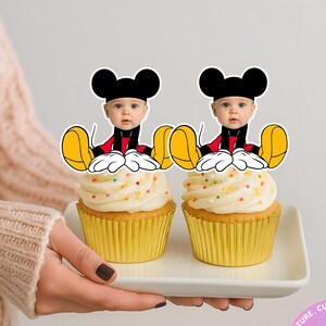 Puede incluir: Dos cupcakes con envoltorios amarillos y glaseado blanco, decorados con chispas de colores. Cada cupcake tiene un adorno con la cara de Mickey Mouse. El texto "PRINTED & SHIPPED" es visible.