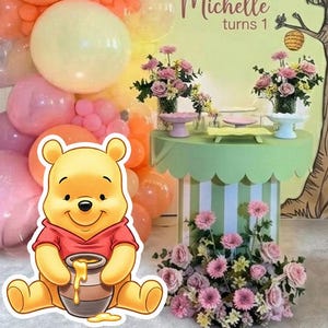 Puede incluir: Escena de fiesta de cumpleaños con un recorte de Winnie the Pooh sosteniendo un tarro de miel. El telón de fondo presenta una ilustración de un árbol y el texto "Michelle turns 1". Globos en rosa, naranja y amarillo decoran la escena, junto con arreglos florales.