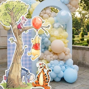 Puede incluir: Una escena de fiesta caprichosa con personajes de Winnie the Pooh. Un árbol con Piglet, Pooh sosteniendo un globo, Eeyore y Tigger en primer plano. Globos pastel en azul, amarillo y melocotón crean un telón de fondo festivo.